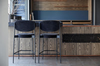 Two black velvet bar stools paired with a textured wooden kitchen backdrop, featuring gray and blue hues.