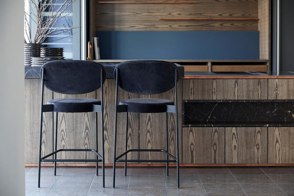 Two black velvet bar stools paired with a textured wooden kitchen backdrop, featuring gray and blue hues.