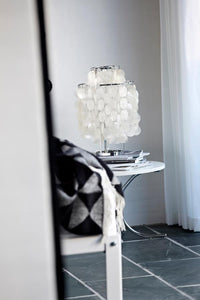 "Elegant white lamp with circular shades on a sleek white table, complemented by a patterned black and white throw."