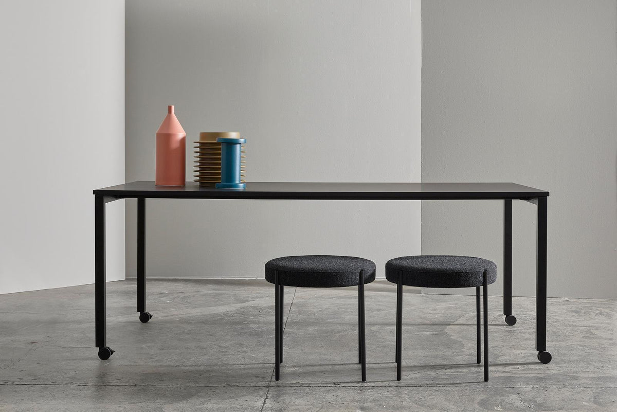 Black table with black legs, gray stools, and vibrant pink, blue, and yellow decor accents. Minimalist design.