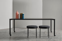 Black table with black legs, gray stools, and vibrant pink, blue, and yellow decor accents. Minimalist design.