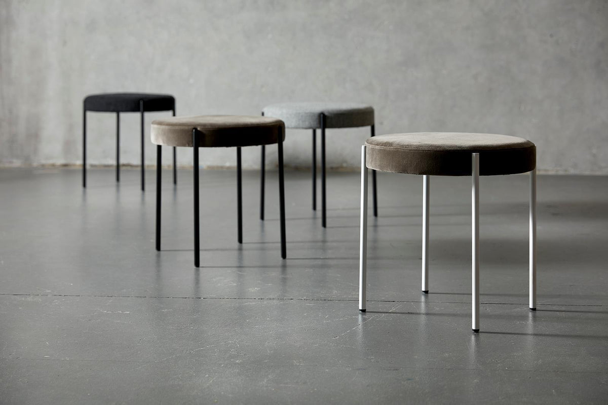 Set of four modern stools in black, gray, and brown tones with soft fabric tops and sleek metal legs.