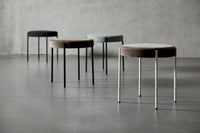 Set of four modern stools in black, gray, and brown tones with soft fabric tops and sleek metal legs.