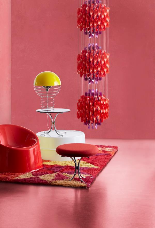 Vibrant red chair, yellow lamp, and colorful rug against a pink backdrop create a bold, modern interior look.