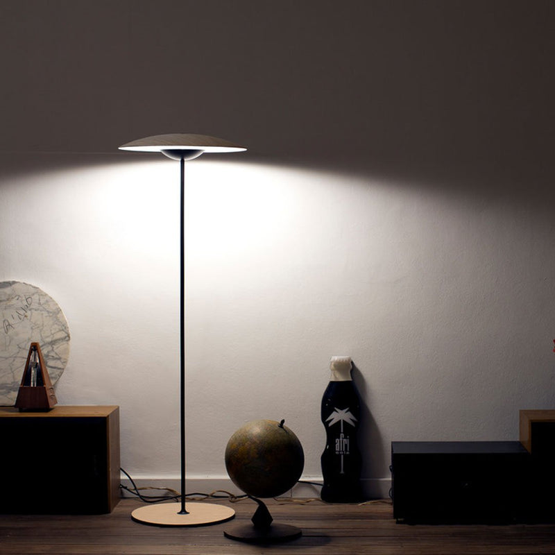 Sleek black floor lamp with a white circular shade, illuminating warm neutral tones and modern aesthetic patterns.