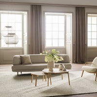 Light gray sofa with beige accents, wooden tables, and soft neutral curtains in a bright, airy room.