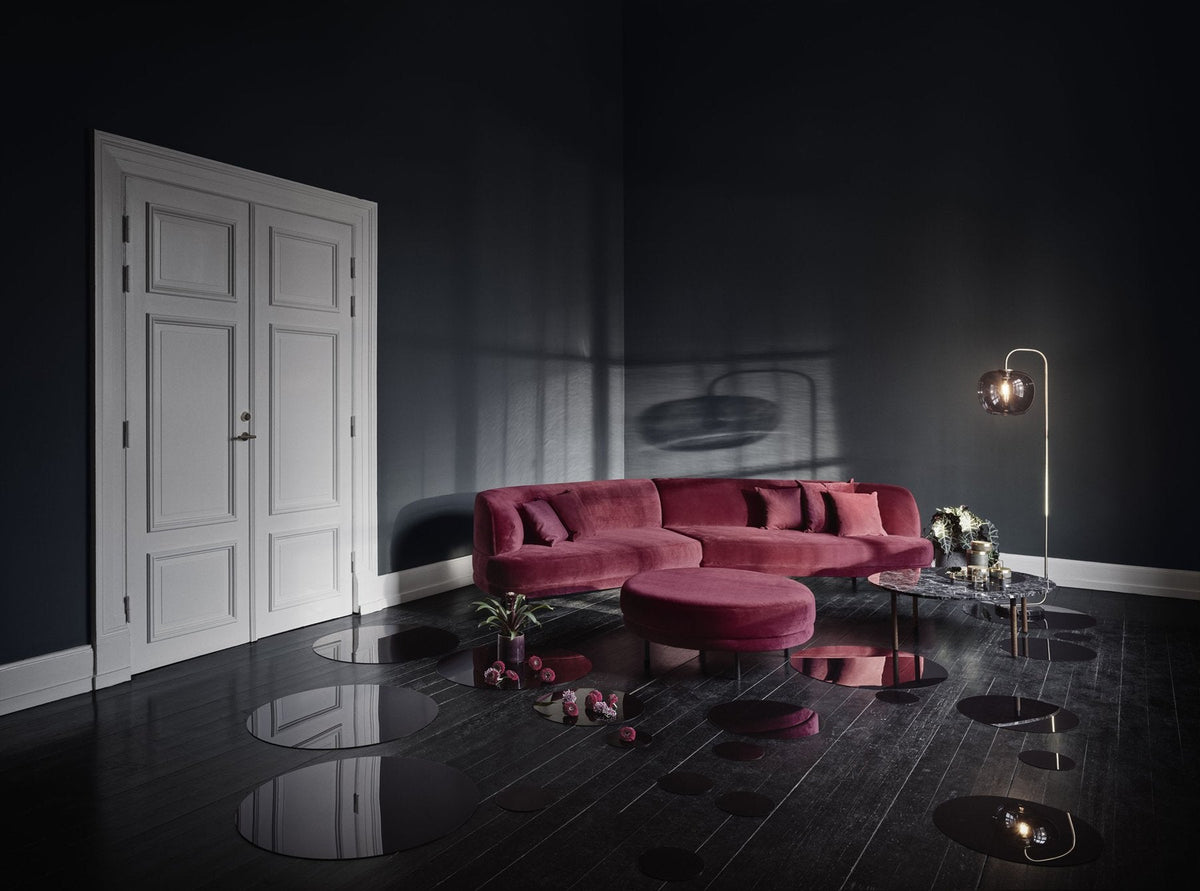 Plush burgundy sofa and round ottoman in a dark, moody room with shiny black floors reflecting dim light.