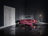Plush burgundy sofa and round ottoman in a dark, moody room with shiny black floors reflecting dim light.