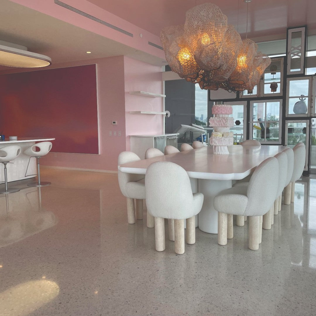 Modern dining room featuring a white table, soft pink walls, and textured hanging light fixtures for a chic look.