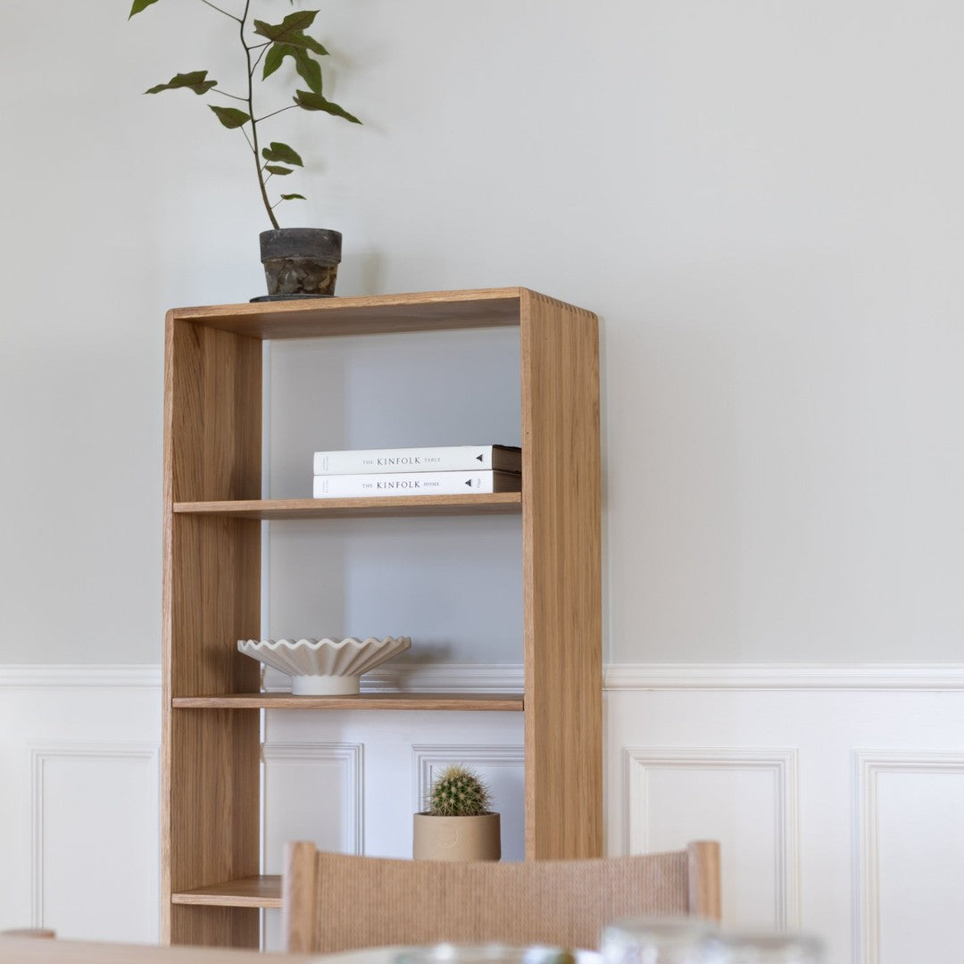 Light oak bookshelf with clean lines against a soft gray wall, featuring minimalist decor and natural greenery.