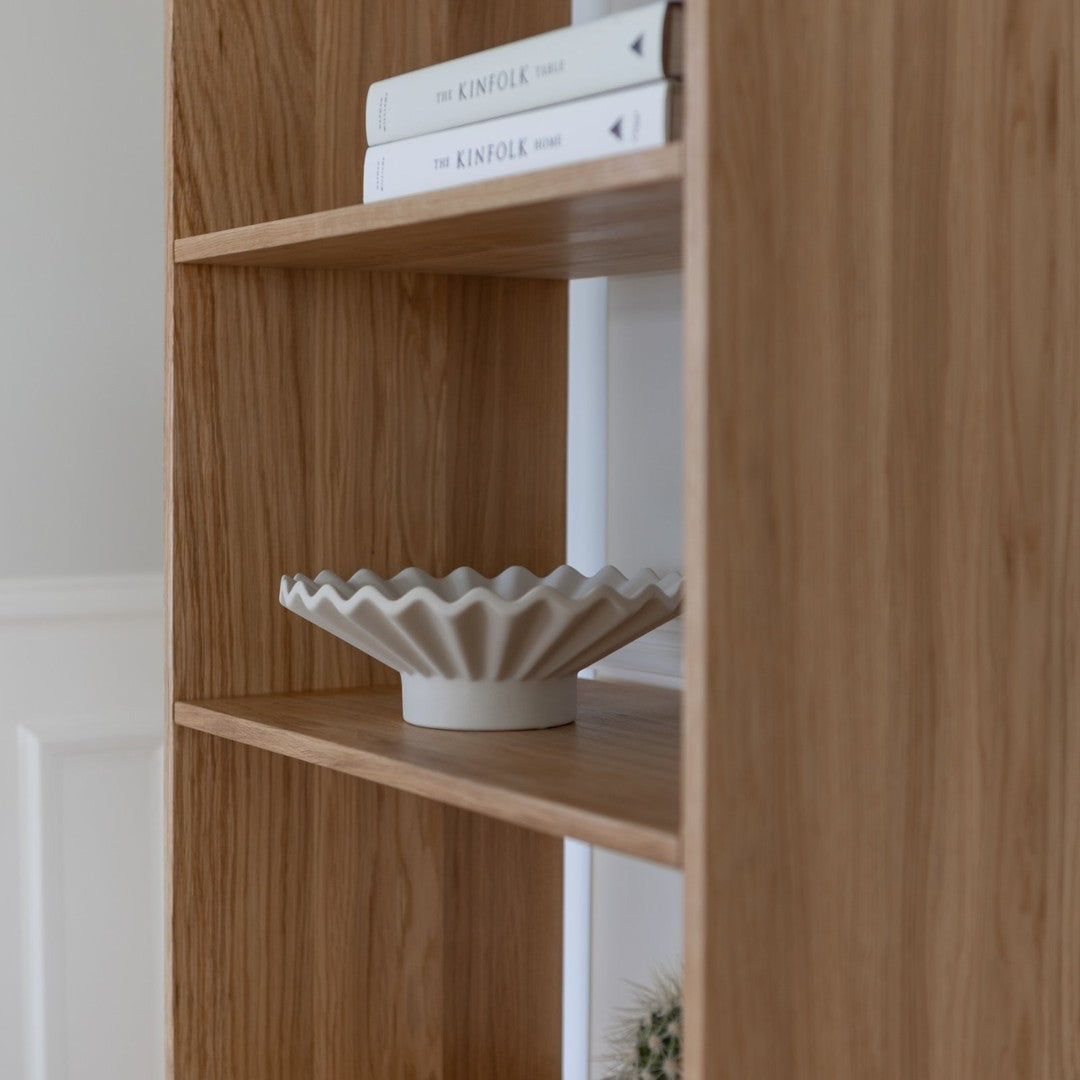 "Light oak wood shelves with a textured white ceramic bowl and stacked books in neutral tones."