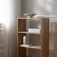 Natural wood bookshelf with light oak finish, featuring clean lines and minimalistic design in a softly lit room.