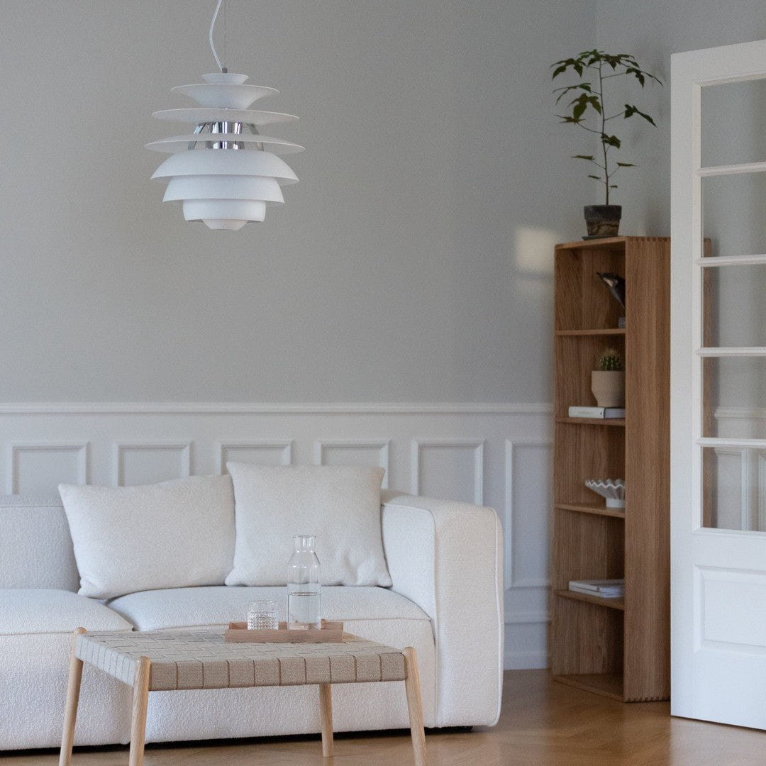 Modern white pendant lamp with layered design, set against neutral gray walls and light wood accents. Elegant, minimalist style.