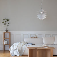 Modern white pendant light with layered design, set against a soft gray wall and natural wood furnishings.