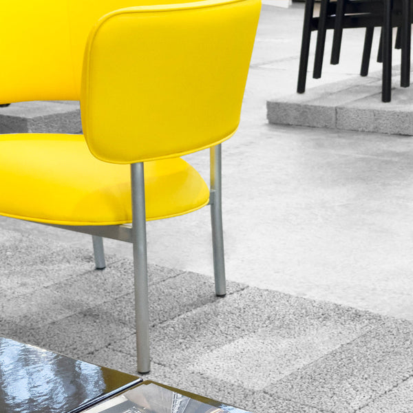 Bright yellow chair with a smooth finish and sleek silver legs, set against a modern gray background.