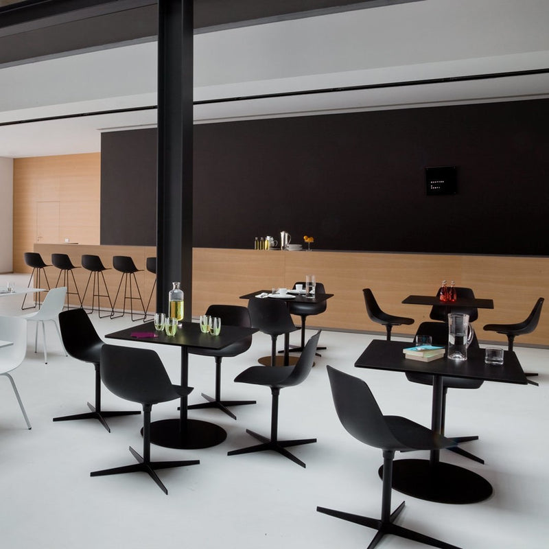 Modern black and white dining area with sleek chairs and tables against a minimalist wood and black backdrop.