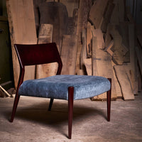 Mid-century modern chair with a rich mahogany frame and soft, textured blue upholstery against a rustic wood backdrop.