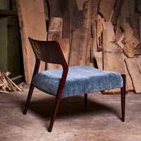 "Velvet blue chair with dark wood legs, featuring a sleek modern design against a backdrop of wooden planks."