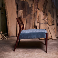 Side view of a blue velvet chair with a rich wooden frame, surrounded by natural wood textures.