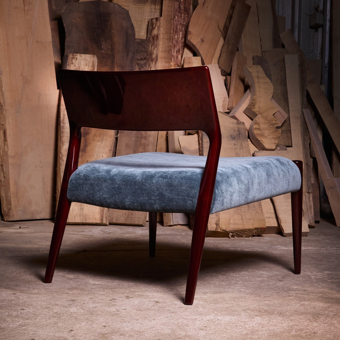 Modern chair with rich mahogany frame and soft blue upholstery against a textured wooden backdrop.
