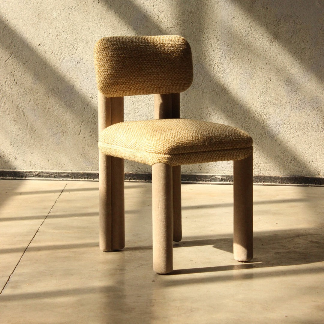 "Beige upholstered chair with a textured fabric and wooden legs, set against a minimalist backdrop."