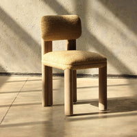 "Beige upholstered chair with a textured fabric and wooden legs, set against a minimalist backdrop."