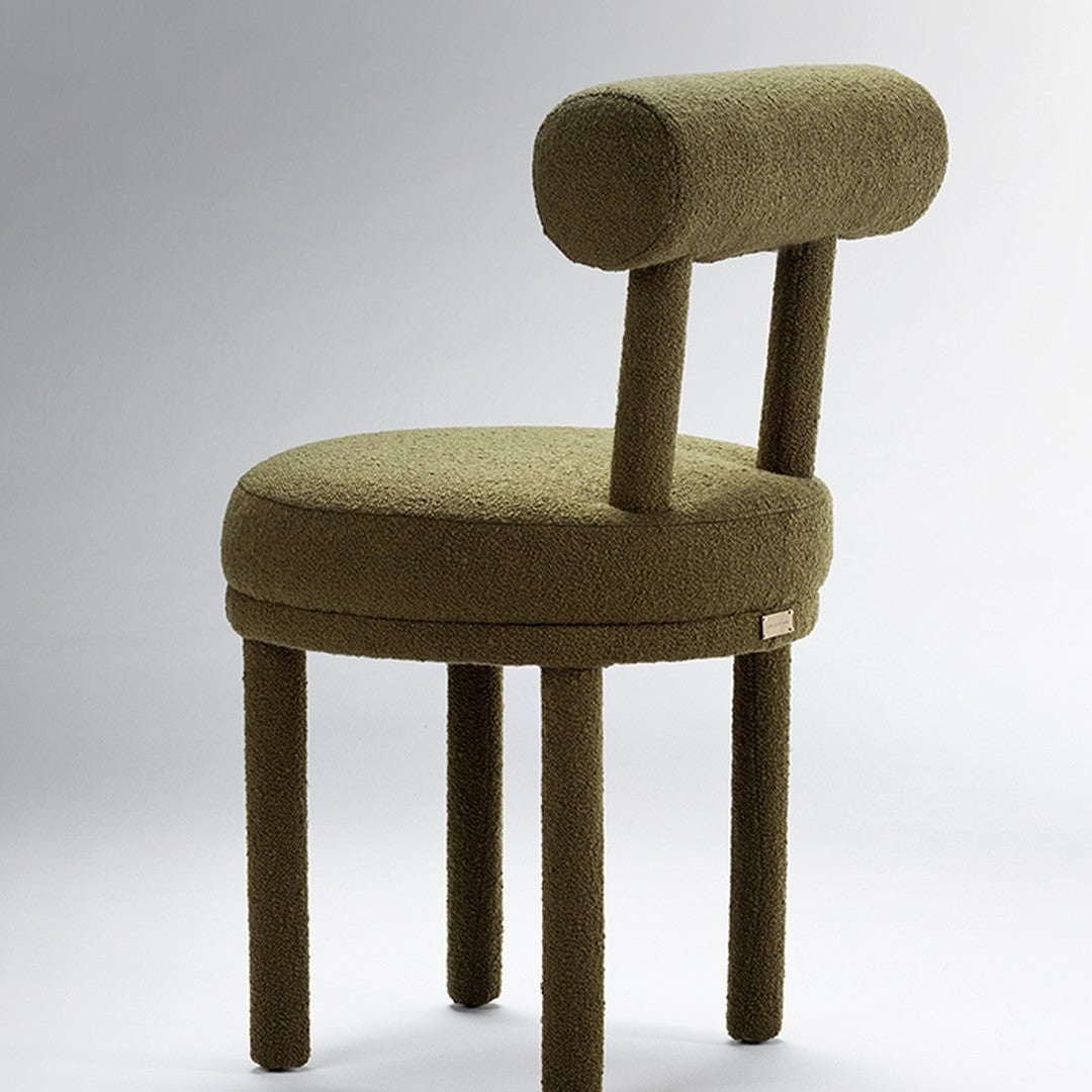 Olive green upholstered chair with a round seat and unique cylindrical backrest design. Soft texture, minimalist style.