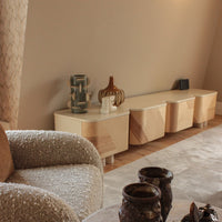 Light wood sideboard with geometric patterns, beige textured chair, and earthy ceramic decor against a neutral background.