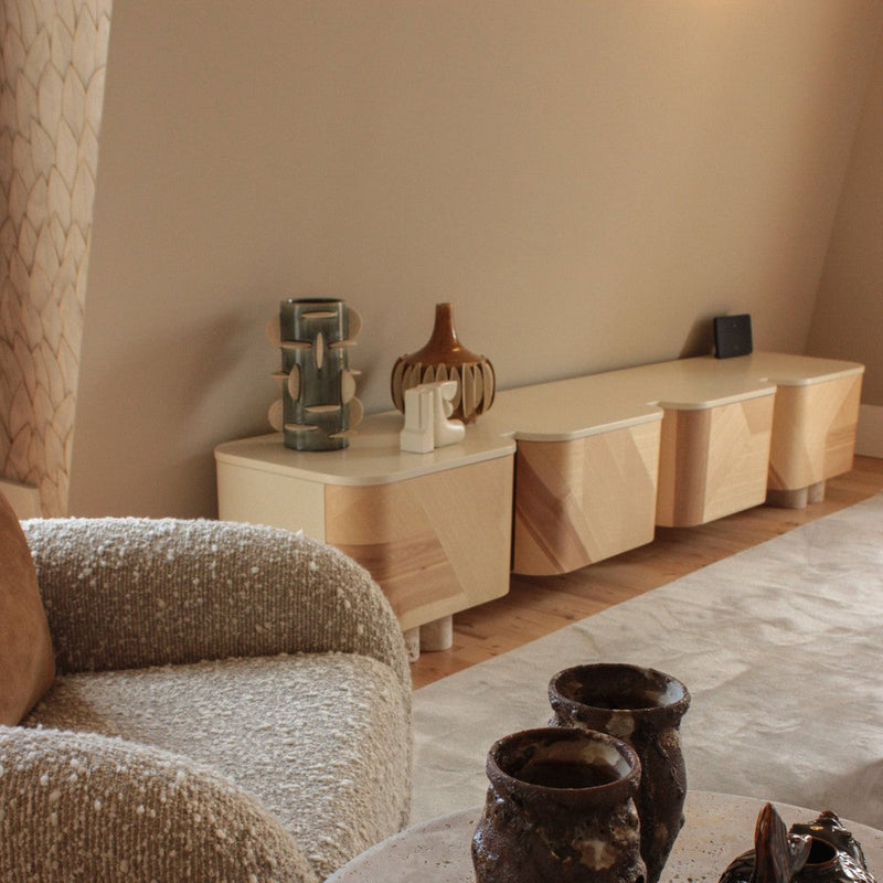 Light wood sideboard with geometric patterns, beige textured chair, and earthy ceramic decor against a neutral background.