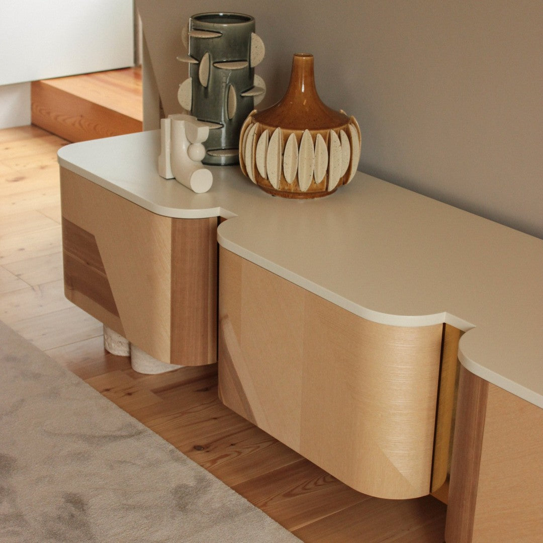 Modern sideboard in light wood with curved edges, complemented by a beige top and colorful decorative vases.