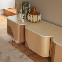 Modern sideboard in light wood with curved edges, complemented by a beige top and colorful decorative vases.