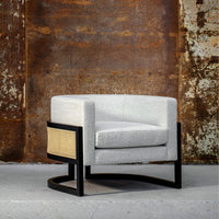 Stylish gray upholstered chair with a woven rattan side, featuring a sleek black frame. Modern design accent.