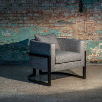 Gray textured chair with black frame against a rustic brick wall backdrop. Stylish and modern design for any space.