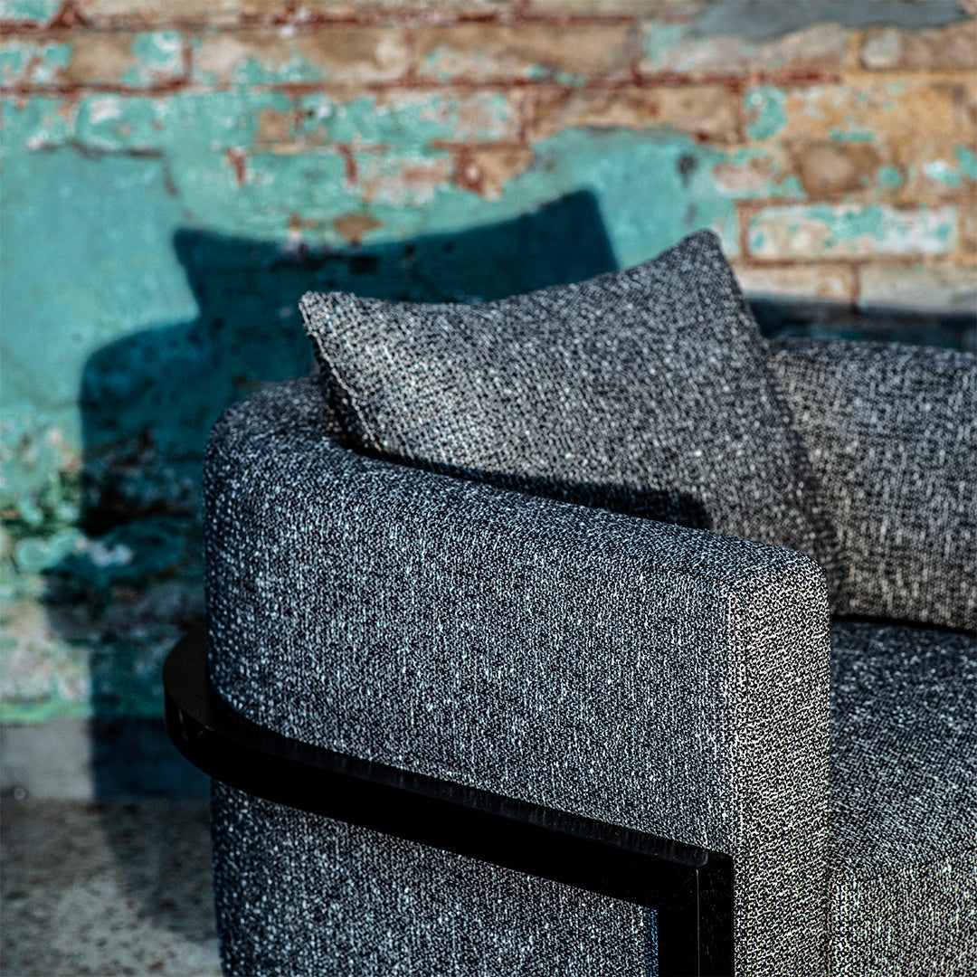 Stylish gray textured sofa with a sleek black frame, featuring a cozy patterned pillow. Perfect modern decor.