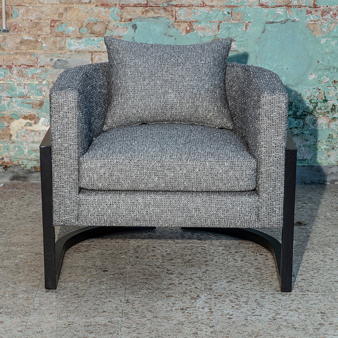 Gray upholstered accent chair with textured fabric and a matching cushion, set against a rustic backdrop.