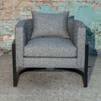 Gray upholstered accent chair with textured fabric and a matching cushion, set against a rustic backdrop.