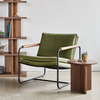 Green velvet chair with black metal frame and wooden armrests, paired with a rustic ribbed wood side table.