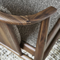 Wooden chair with a rich walnut finish and soft, textured gray upholstery in a neutral-toned patterned rug background.