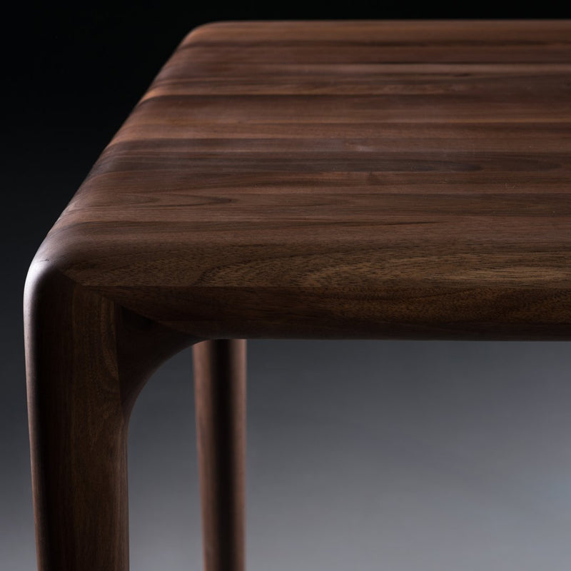 Solid walnut table with rich brown tones and smooth, curved edges, showcasing a sleek, modern design.