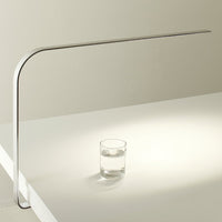 Sleek silver desk lamp with minimalist design casting warm light on a clear glass of water.