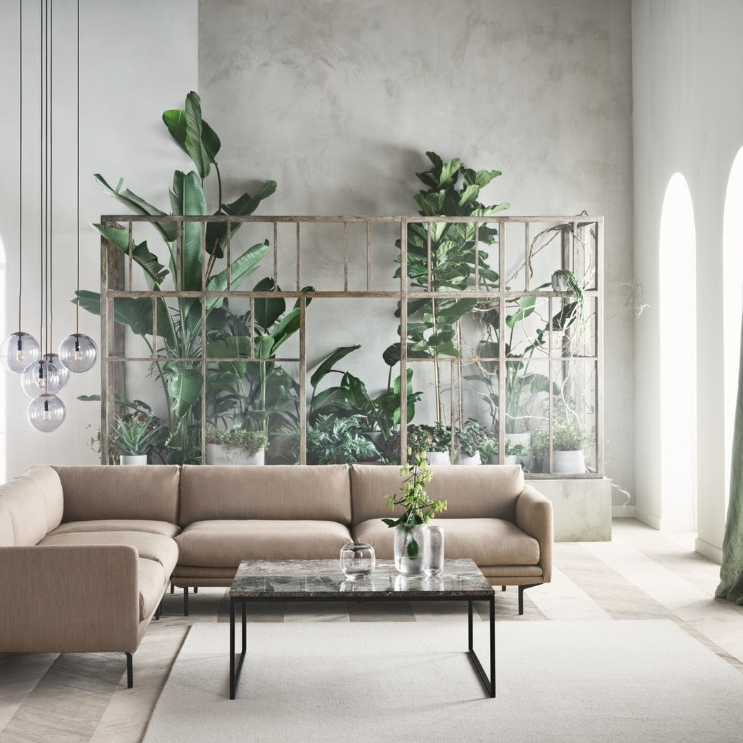 Beige sectional sofa, glass-topped coffee table, and green foliage create a serene, modern living space ambiance.