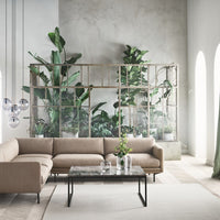 Beige sectional sofa, glass-topped coffee table, and green foliage create a serene, modern living space ambiance.