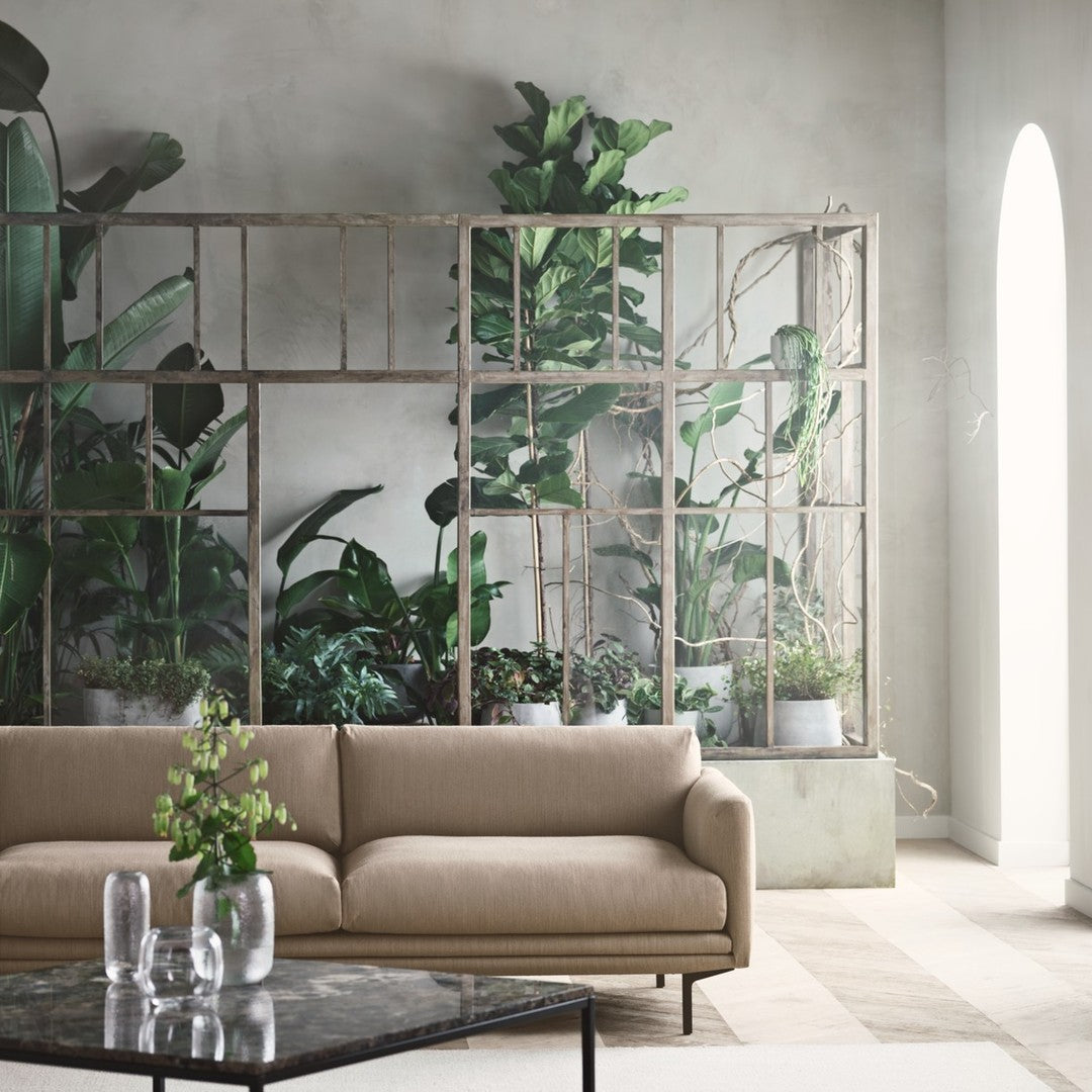 "Neutral beige sofa in a modern interior with lush green plants and light gray walls."