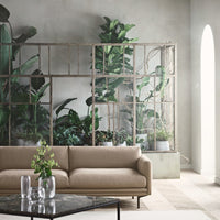 "Neutral beige sofa in a modern interior with lush green plants and light gray walls."