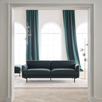 Modern black sofa with sleek lines, complemented by rich teal curtains and a neutral beige floor.