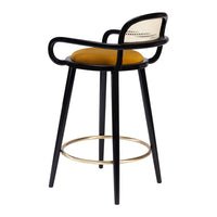 Black bar stool with woven backrest and mustard yellow seat cushion, accented by a sleek gold footrest.