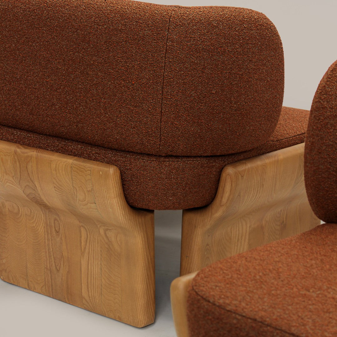 Rust-colored upholstered sofa with a textured pattern and natural wood base. Modern design with rounded edges.