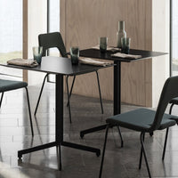 Two minimalist black tables with green upholstered chairs, glassware, and natural wood accents. Modern, sleek design.