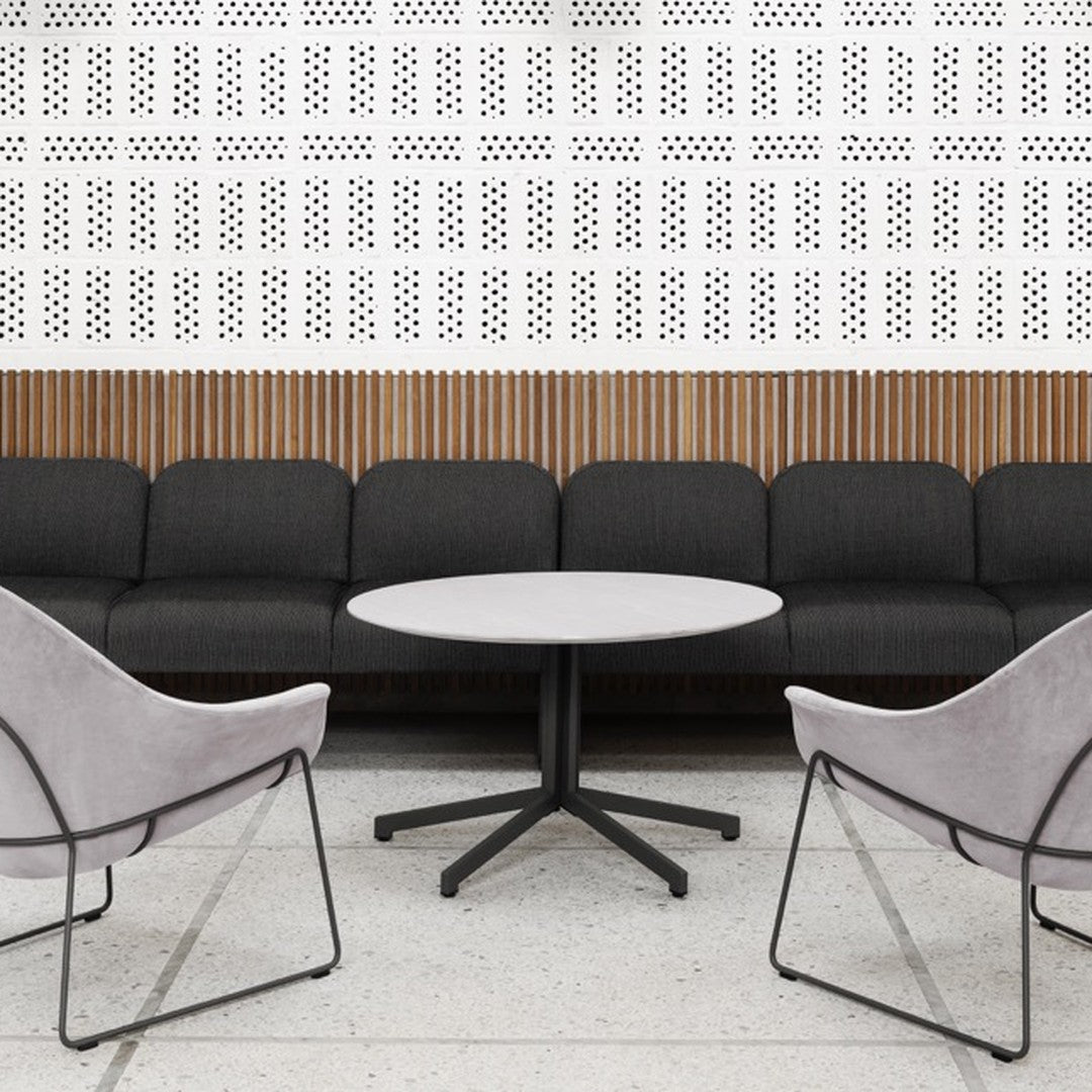 Black textured sofa, light grey round table, and soft pink chairs against a white patterned wall with wooden accents.