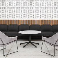 Black textured sofa, light grey round table, and soft pink chairs against a white patterned wall with wooden accents.